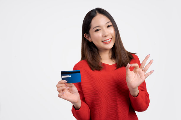 亚洲女人微笑着拿着信用卡在一个白色的背景。图片下载