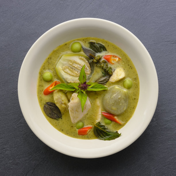 著名的国际知名的泰国绿色椰子咖喱'Gaeng Keow Wan Gai'，鸡肉，在一个白色的碗，坐在黑暗的石板背景。图片下载