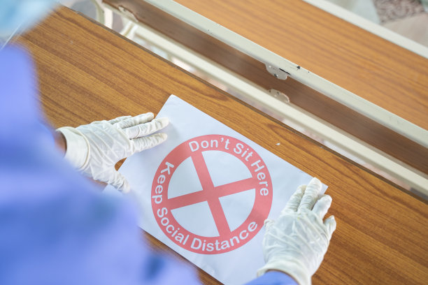 戴着医用口罩和手套的人的肩部照片不要坐在这里，保持社交距离标志海报在桌面上，作为学校或大学的冠状病毒或covid-19安全措施图片下载