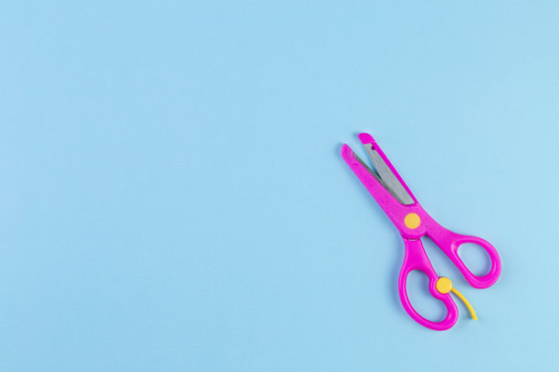 蓝色背景上的粉色儿童剪刀的极简主义照片。图片下载