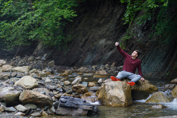 一个年轻人用手机在石头上拍自己的照片。图片下载