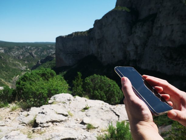 这是一个徒步者在野外徒步时一边看手机，一边以山顶为背景的手拍照片图片下载