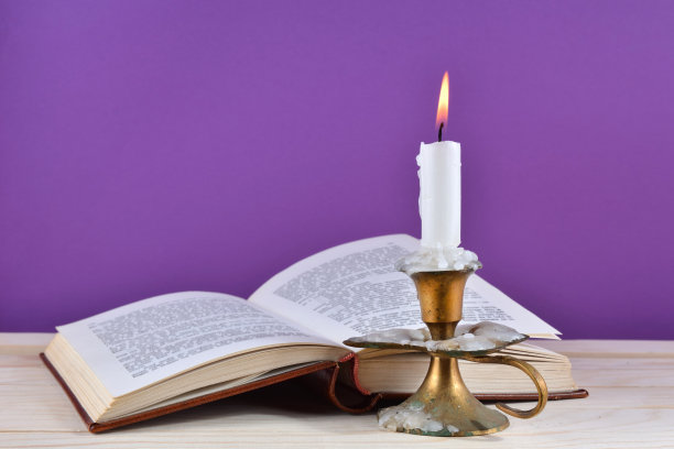 蜡烛燃烧在旧烛台和打开的书在书桌上孤立的紫色背景图片下载