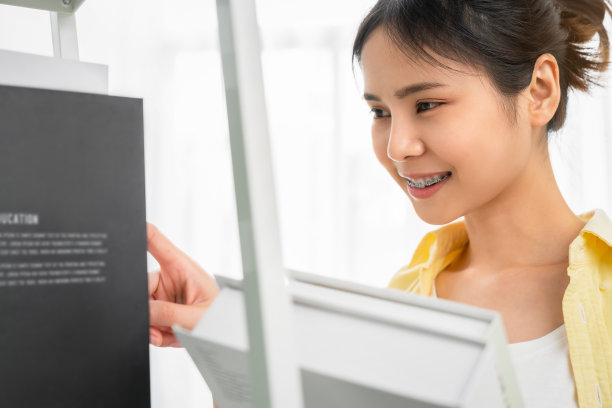 亚洲女学生手里拿着一本书，正在从书架上选择一篇论文来阅读。图片下载