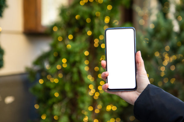 女人手持电话与白色屏幕的圣诞树在背景图片下载