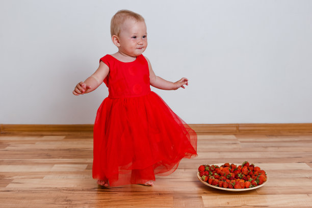 快乐的女孩穿着一件红色的光着脚的裙子和草莓图片下载