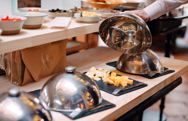 在带帽的金属碗上切奶酪。酒店或餐厅早餐。图片下载