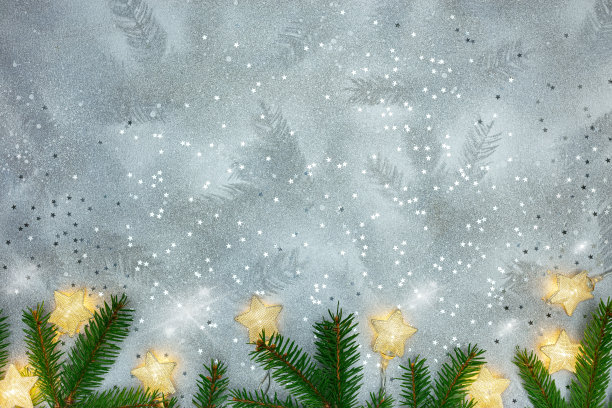 绿色的圣诞树枝与发光的星星花环在银色的背景图片下载