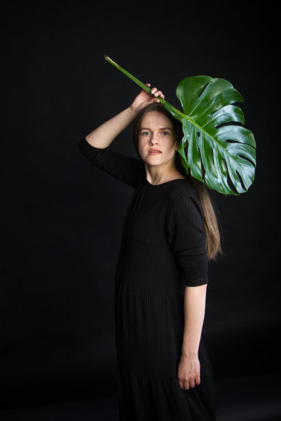 美丽的黑发女孩与明亮的绿色热带树枝，女孩与怪物的叶子在黑色的背景图片下载