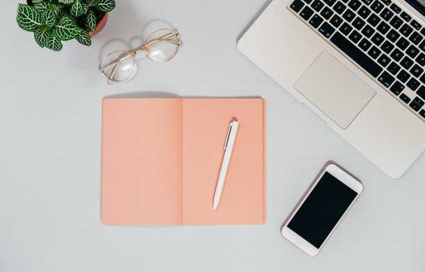 俯视图的办公桌与笔记本电脑，手机，桃子笔记本和植物在灰色背景库存照片图片下载