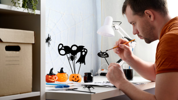 为万圣节做准备。DIY的概念。一个人把一张南瓜纸涂成黑色，作为万圣节的装饰品放在桌子上，室内。图片下载