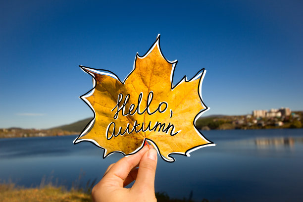 手握枫叶，手握秋叶，用手写文字招呼秋日，映衬着蓝天和湖水图片下载