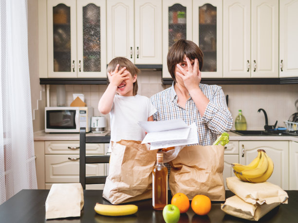 家人在厨房里整理购买的东西。父亲和儿子展示了购物袋里昂贵的产品。因冠状病毒感染的隔离条件下的食品杂货配送。图片下载