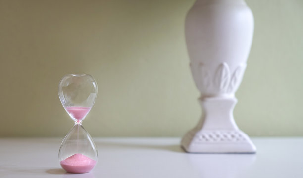 桌子上的沙玻璃有柔和的绿色背景。测量时间的流逝，倒计时或日常的概念。图片下载