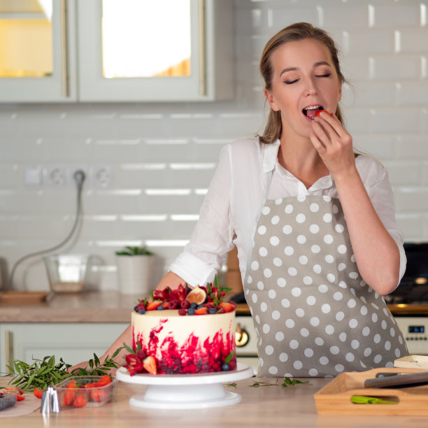 用奶油烹饪和装饰蛋糕。年轻的糕点师在厨房里装饰红丝绒蛋糕图片下载