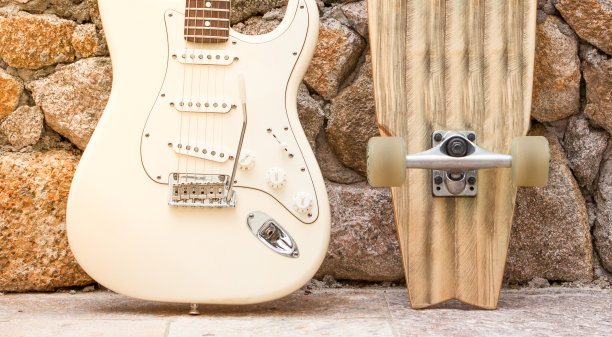 靠在石墙上的吉他和滑板的身体图片下载