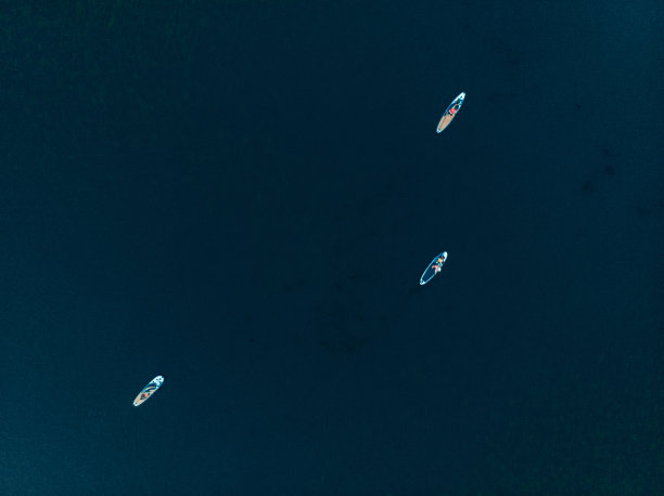 游客在湖上的顶视图与supboard。美丽清澈的水，人们在冲浪板上浮动。在背景地平线上划船的人的海景图片下载