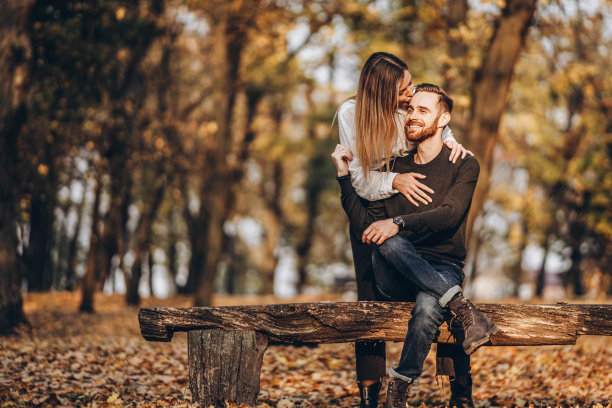 一对年轻的情侣坐在森林里的一张木凳上。图片下载