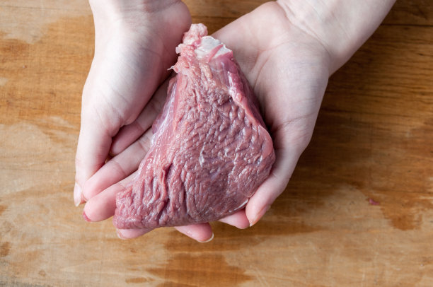 女人的手拿着一块木头背景上的生牛肉图片下载