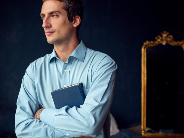 一个年轻人在读一本书，一个穿着蓝色衬衫和深蓝色背景的人。图片下载