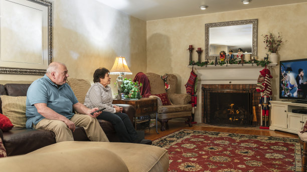 这对老夫妇坐在客厅壁炉前的沙发上，一起看电视屏幕上的家庭圣诞照片。丈夫用遥控器切换频道。图片下载