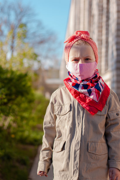一名女孩戴着粉色防护口罩，防止COVID-19冠状病毒病隔离。停止流行街头照片。图片下载