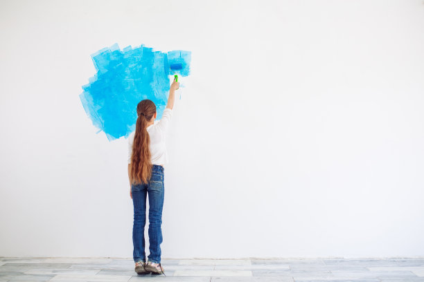 在公寓里修理。快乐的小女孩用蓝色的油漆涂墙，图片下载