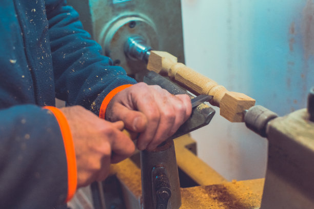 男人的手拿着凿子靠近车床，男人在小木车床上工作，一个工匠用手工车床雕刻一块木头图片下载