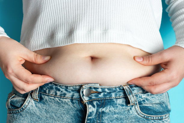 女人的手握过多的腹部脂肪在蓝色背景。图片下载