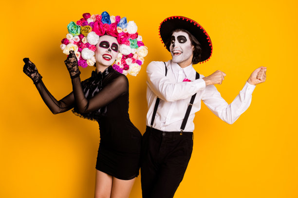 搞笑的两人照片男人女人新娘跳舞伦巴做拉丁动作节日穿黑色的迷你裙死亡服装玫瑰头带吊带帽孤立的黄色背景图片下载