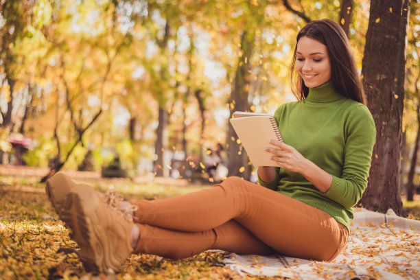 可爱的照片可爱的女士大学老师坐毯子拿抄写准备演讲课程微笑的地方在树林秋天的公园穿绿色的高领毛衣橙色的裤子运动鞋在户外图片下载