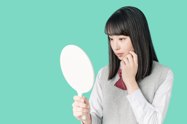 亚洲女学生检查她的皮肤。图片下载