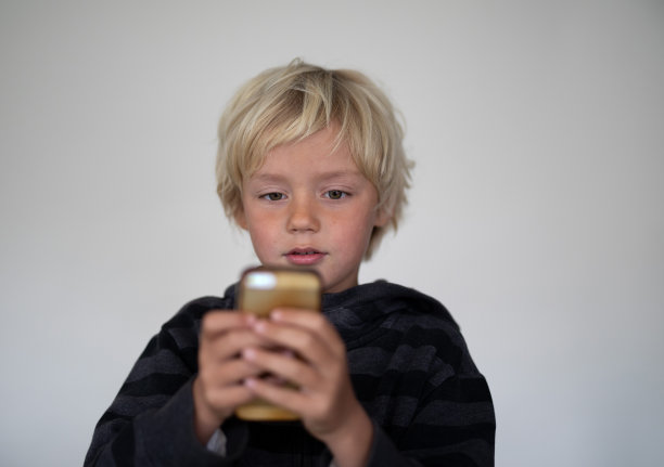 一个小男孩在一个白色屏幕前摆姿势。他们手里拿着一个手机图片下载