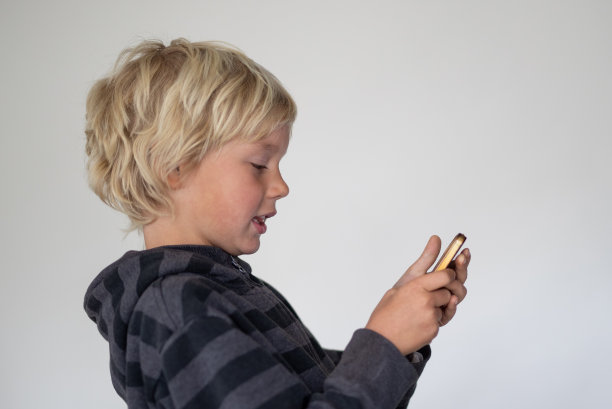 一个小男孩在一个白色屏幕前摆姿势。他们手里拿着一个手机图片下载