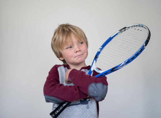 一个小男孩拿着一个旧网球拍在一个白色屏幕前摆姿势图片下载