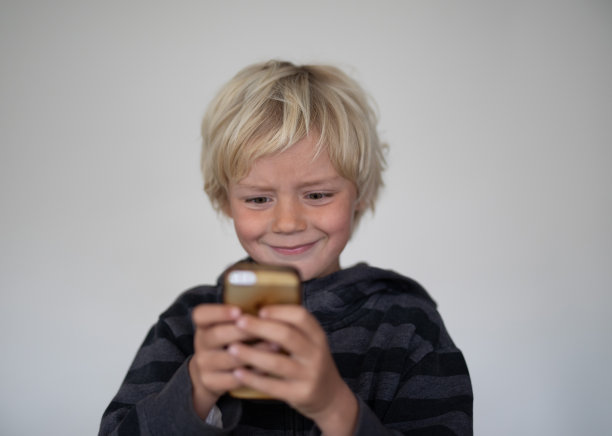 一个小男孩在一个白色屏幕前摆姿势。他们手里拿着一个手机图片下载