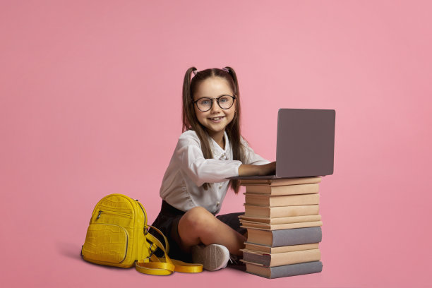 面带微笑的女孩戴着眼镜，背着背包，坐在一堆书和笔记本电脑旁边图片下载