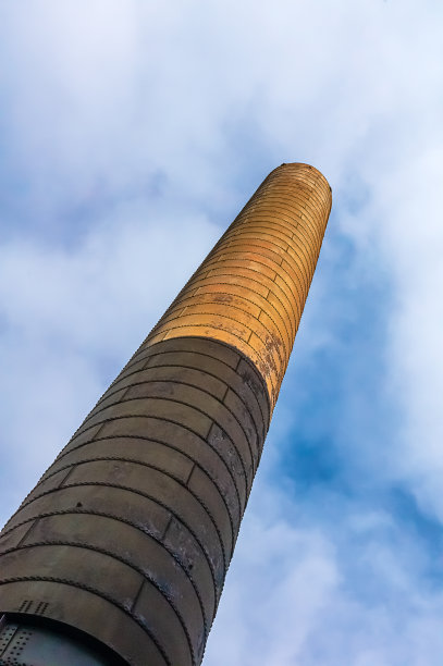 在多云的蓝天下，一个废弃工厂烟囱的角度视图图片下载