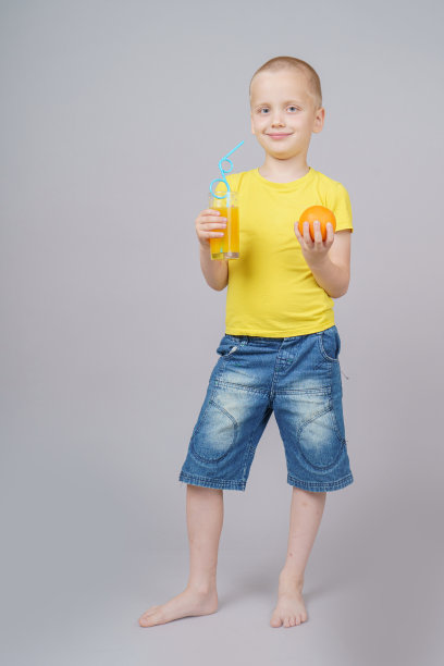 微笑的男孩站在水果，橘子和饮料。孤立在灰色图片下载