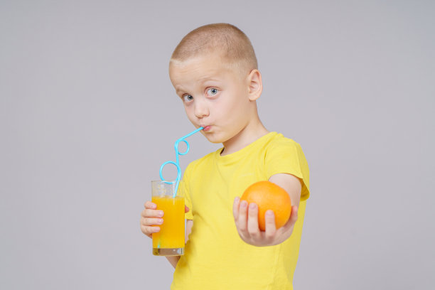 微笑的男孩站在水果，橘子和饮料。孤立在灰色图片下载