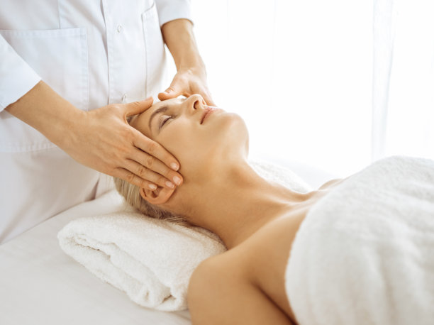 美丽的金发女子在闭着眼睛享受面部按摩。放松治疗的医学和水疗中心的概念图片下载