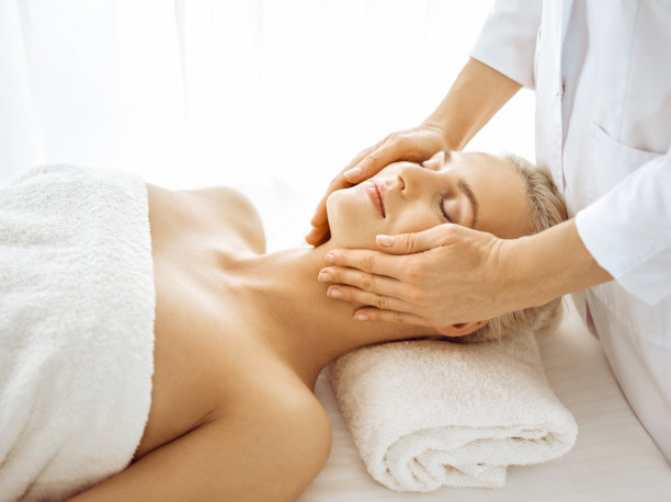 美丽的金发女子在闭着眼睛享受面部按摩。放松治疗的医学和水疗中心的概念图片下载