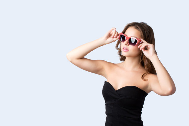 华丽优雅的女人穿着黑色的衣服，戴着墨镜在灰色的工作室摆姿势。图片下载