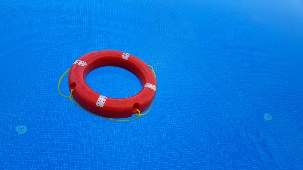亮红色的圆形救生环漂浮在亮蓝色的清澈水潭上图片下载