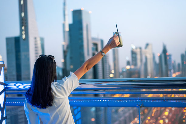 女孩在迪拜欣赏城市天际线，喝着饮品图片下载