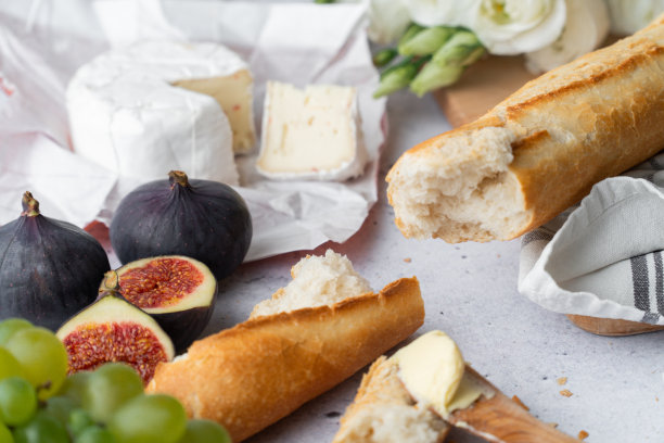 健康的早餐桌上有面包和水果。法式长棍面包，无花果，葡萄，法国奶酪，放在白色的大理石桌子和一块木板上。图片下载