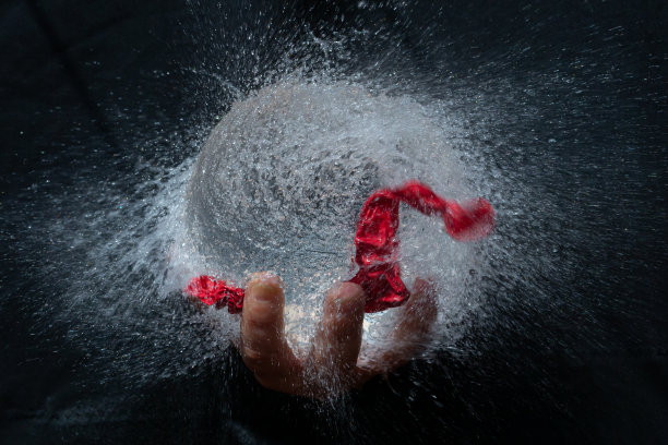 黑色背景下，一只手拿着水球爆炸图片下载