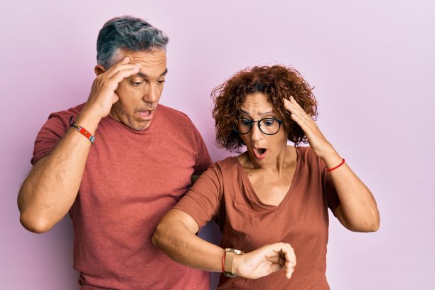 漂亮的中年夫妇一起穿着休闲的衣服看着手表，时间着急，怕迟到图片下载