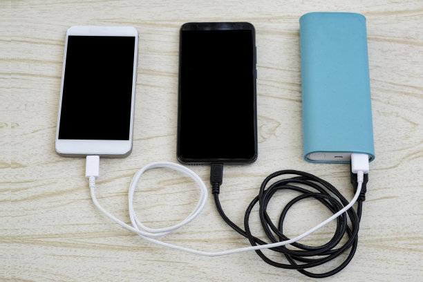两款智能手机——黑色和白色——从桌子上的蓝色电源充电图片下载