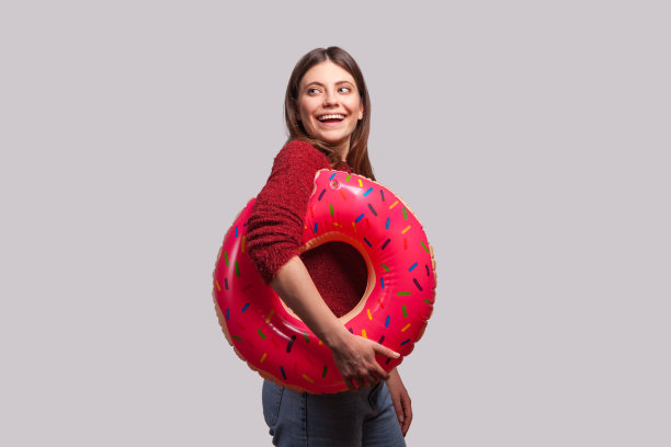 快乐的漂亮女孩走着橡胶圈和粉红色的甜甜圈，望着别处开心地微笑，准备夏天图片下载